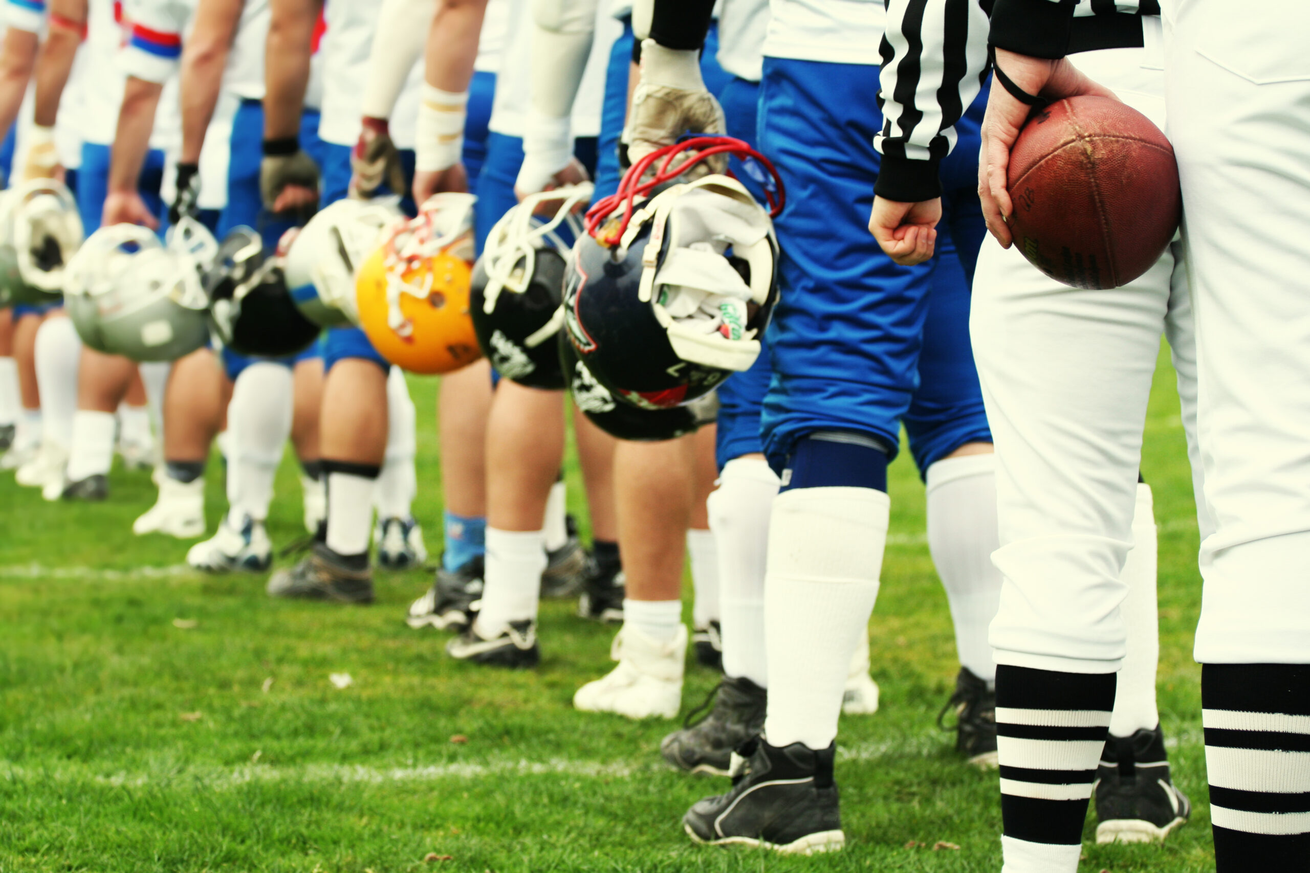 Reihe von Footballspielern in Uniform, die auf dem Spielfeld stehen, mit Helmen und einem Schiedsrichter im Vordergrund.