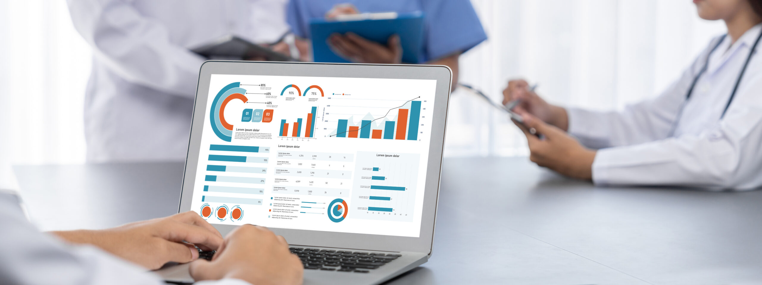 Ein Laptop zeigt grafische Datenanalysen; im Hintergrund stehen medizinisches Personal mit Notizen und Tablets.