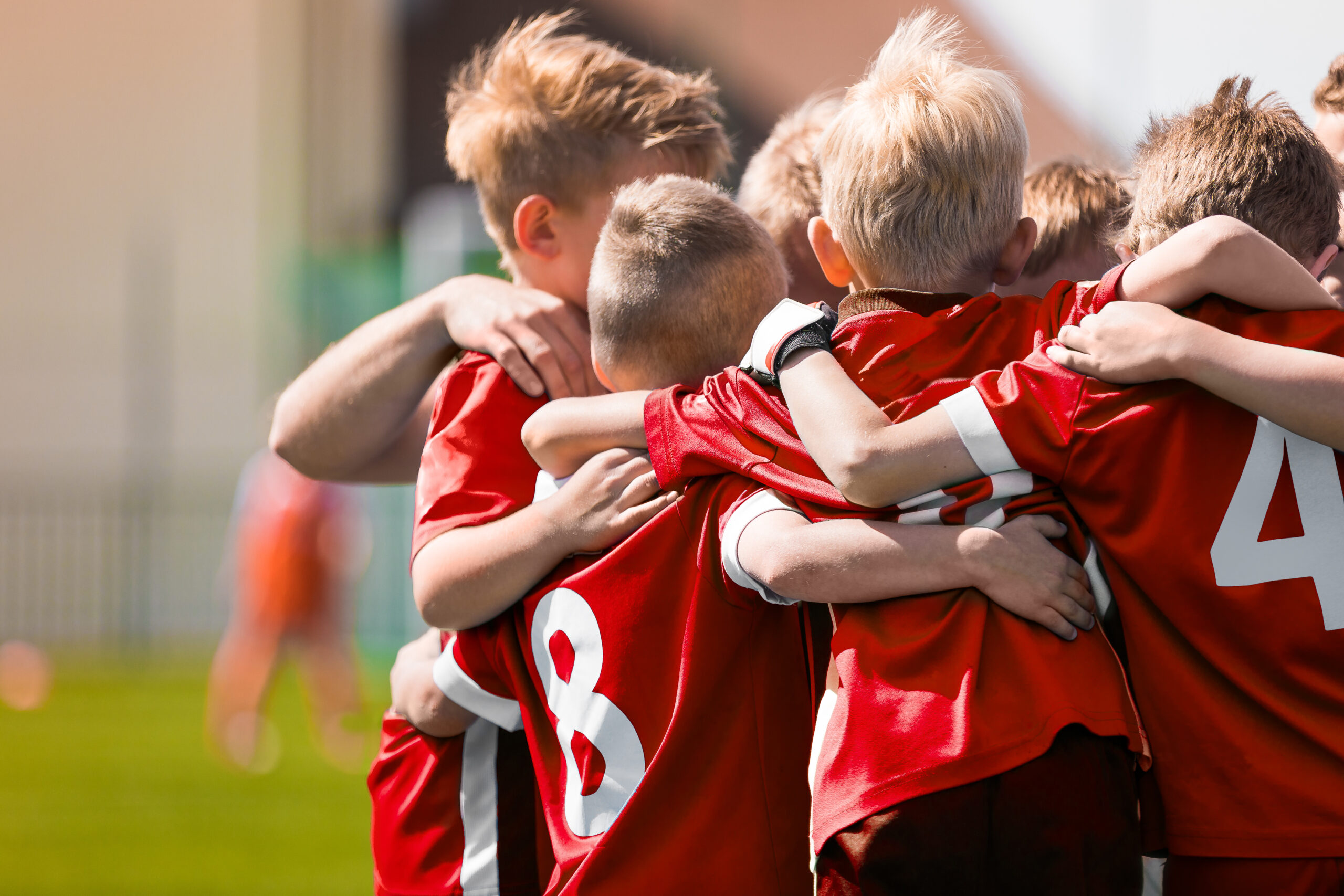 Eine Gruppe von Kindern in roten Trikots umarmt sich auf einem Fu&szlig;ballplatz.