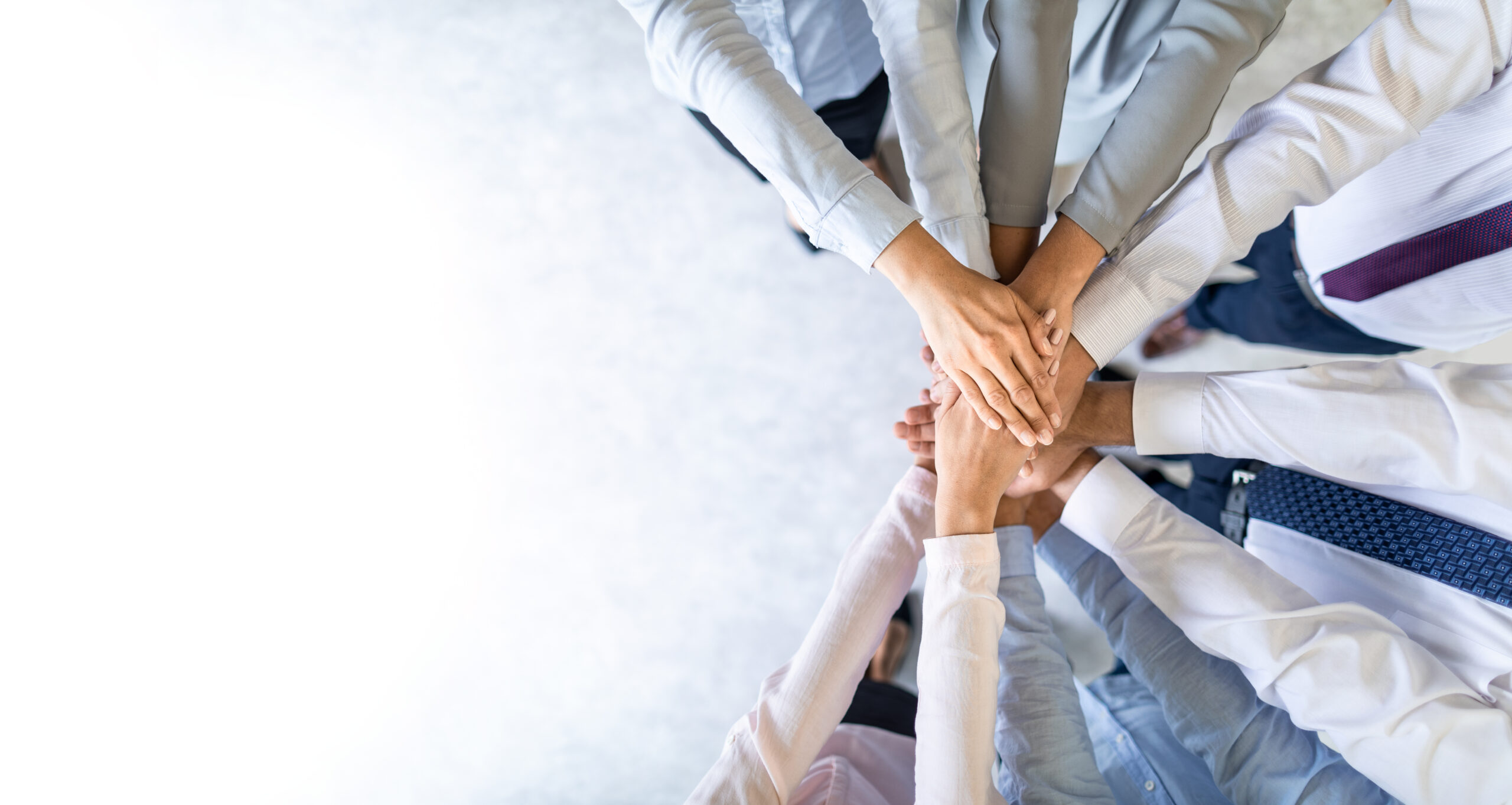 Mehrere H&auml;nde von Menschen in Anz&uuml;gen, die &uuml;bereinander liegen, symbolisieren Teamarbeit und Zusammenarbeit.