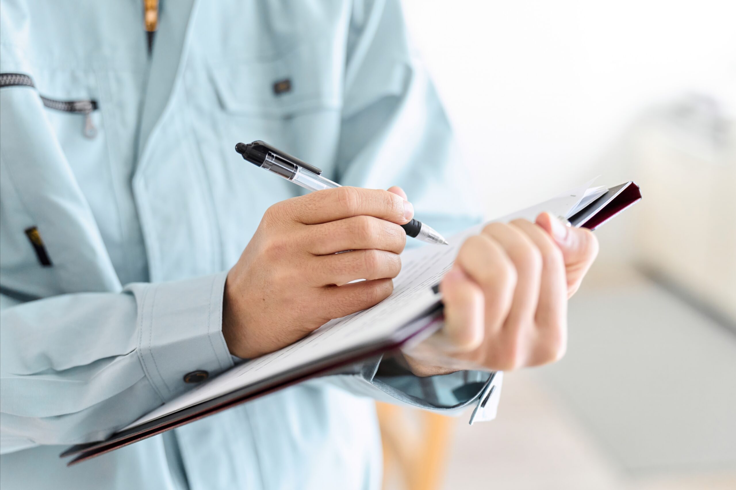 Eine Person in blauer Arbeitskleidung schreibt mit einem Stift in ein Notizbuch.